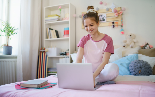 Young girl with laptop sitting and relaxing on bed, quarantine concept.