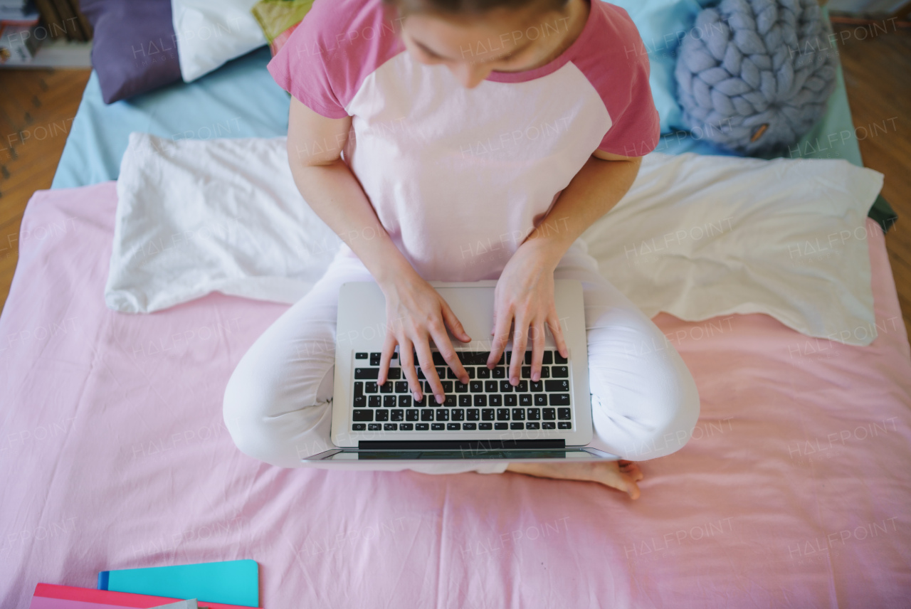 Top view of unrecognizable young girl with laptop on bed, working during quarantine.