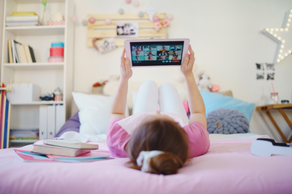 Rear view of young girl with tablet on bed, relaxing during quarantine. Copy space.