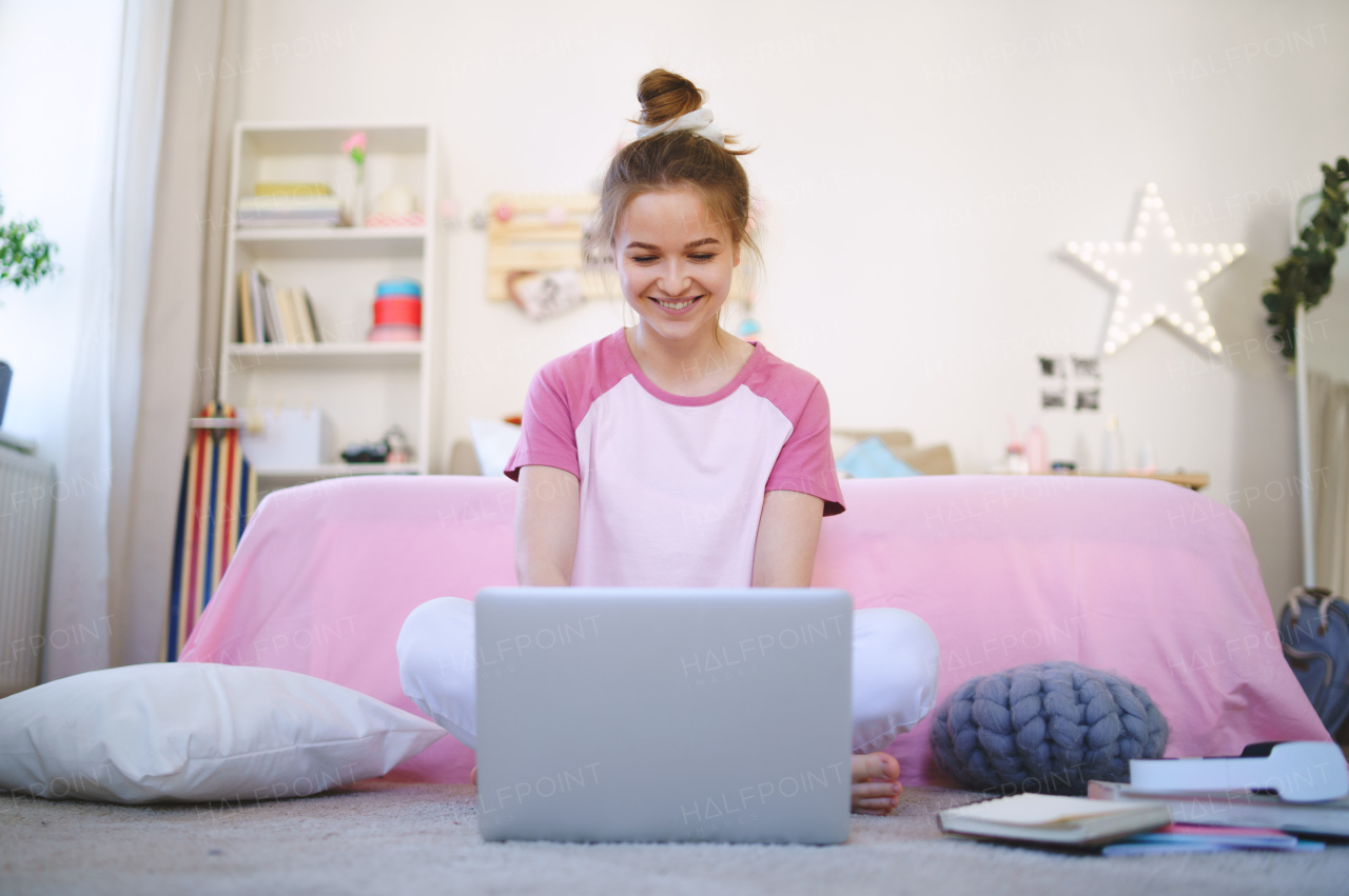 Front view of young girl with laptop sitting on floor, relaxing during quarantine.