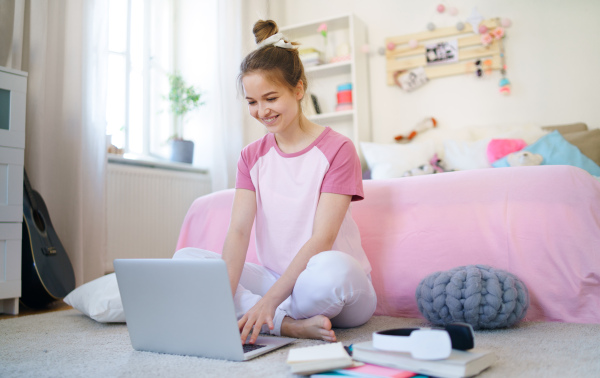 Front view of young girl with laptop sitting on floor, relaxing during quarantine.