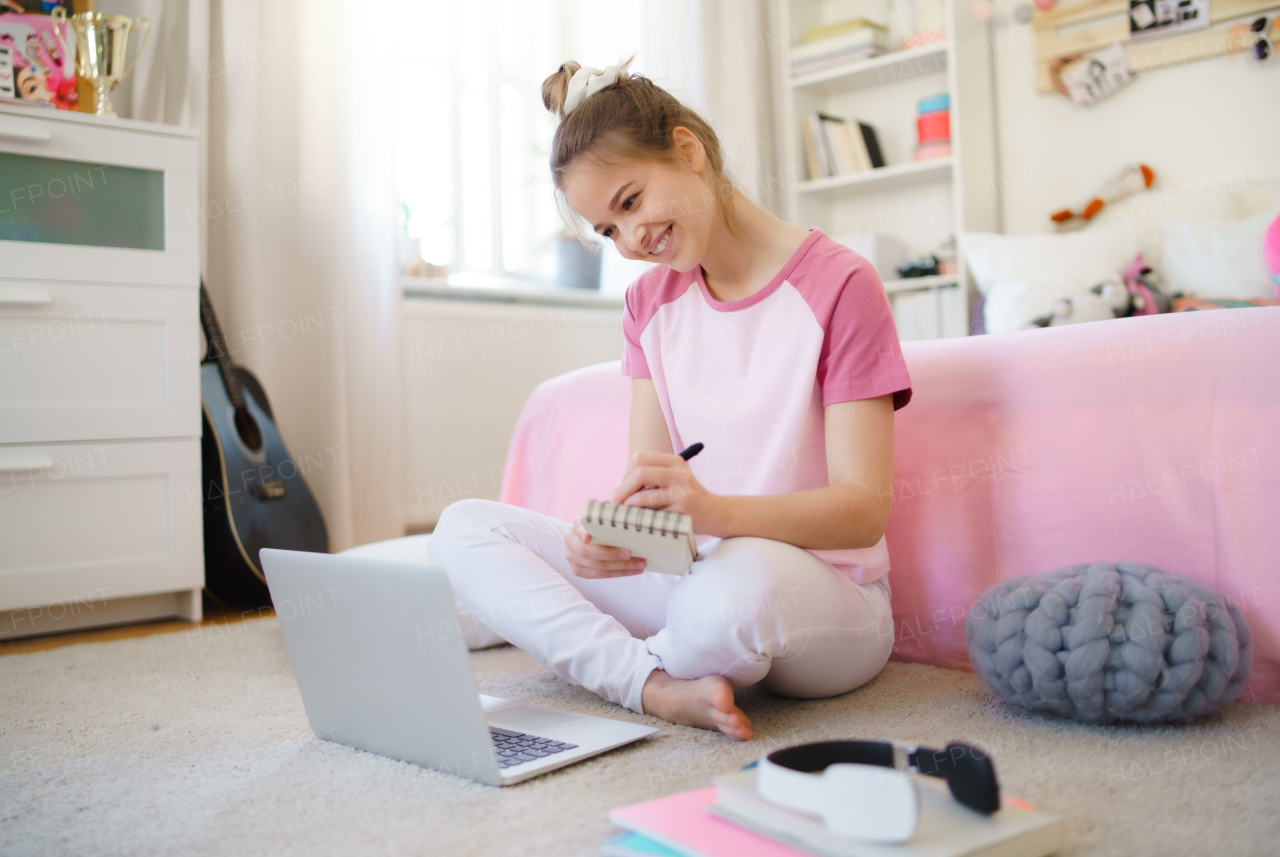 Front view of young girl with laptop sitting on floor, learning during quarantine.