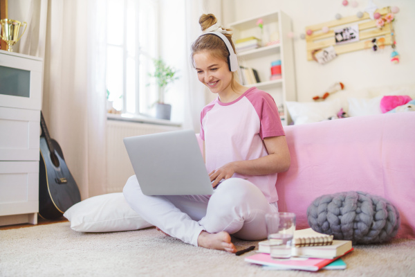 Front view of young girl with laptop and headphones sitting on floor, relaxing during quarantine.