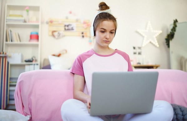 Front view of young girl with laptop and headphones sitting on floor, relaxing during quarantine.