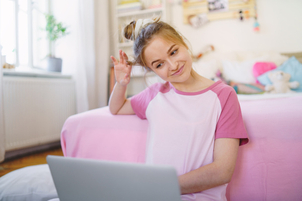 Front view of young girl with laptop sitting on floor, relaxing during quarantine.