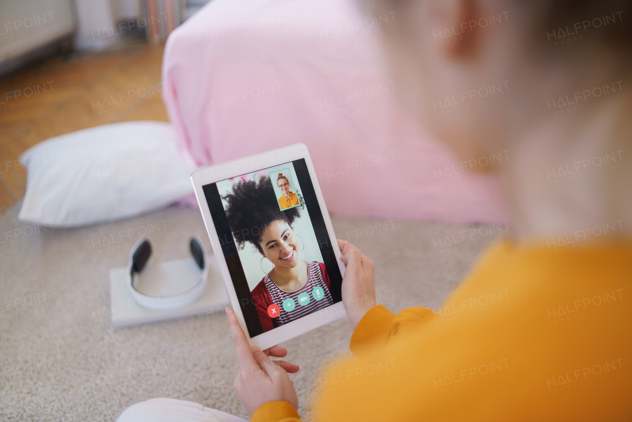 Unrecognizable young student girl with tablet sitting at home, making video call.