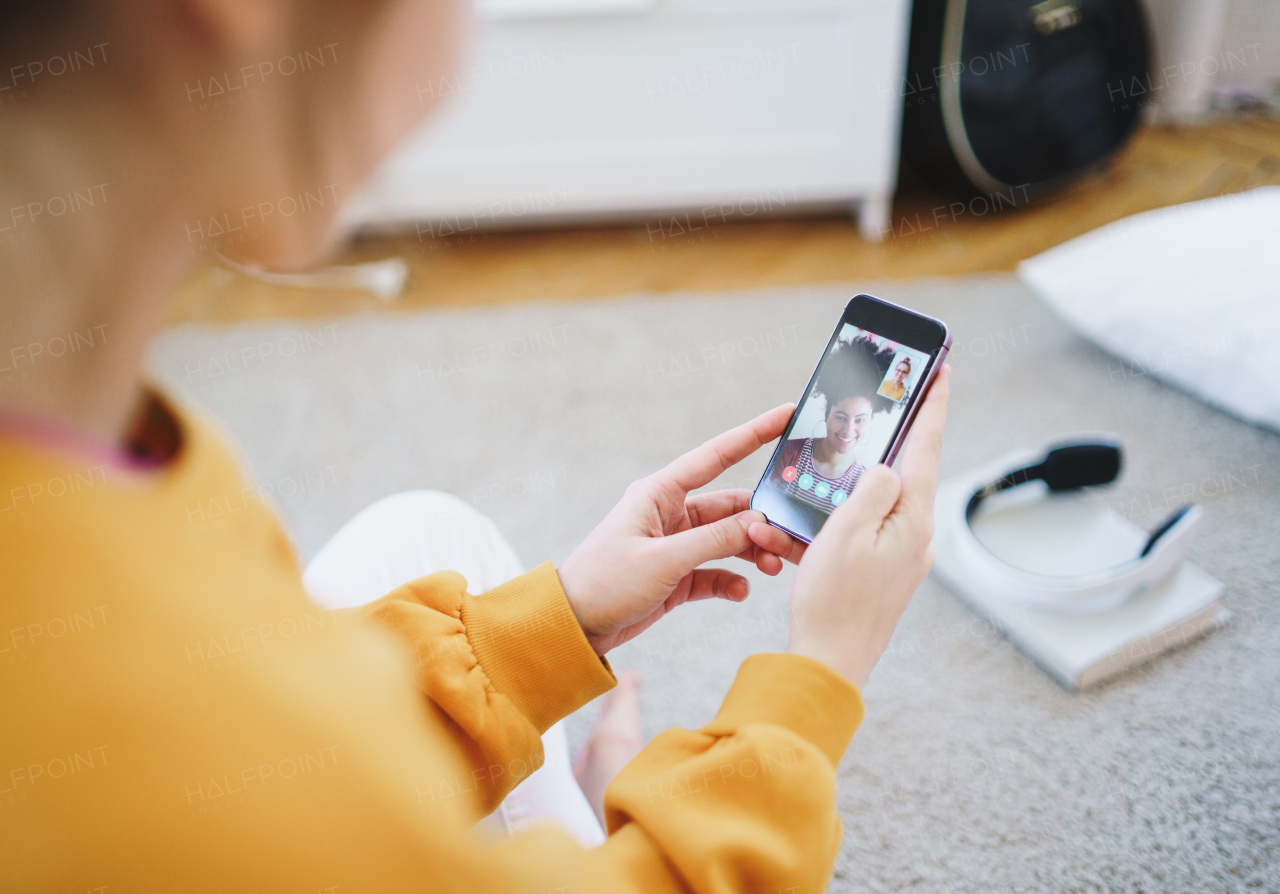 Unrecognizable young girl with smartphone sitting at home, making video call with friend.