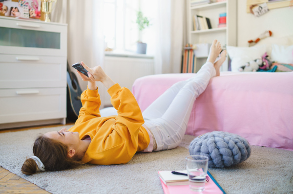 Happy young girl with smartphone on floor at home, making video call.