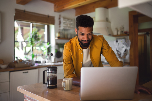 A young man with laptop and coffee working indoors, home office concept.