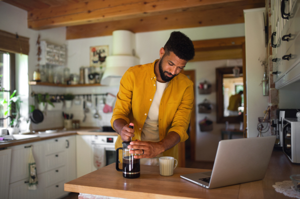 A young man with laptop and coffee working indoors, home office concept.