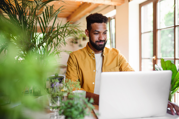 A young man with laptop and coffee working indoors, home office concept.