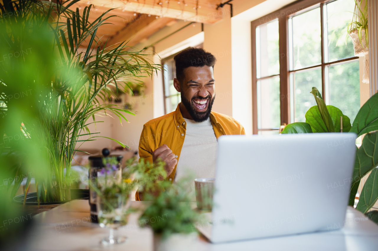 A cheerful young man with laptop working indoors, home office concept.