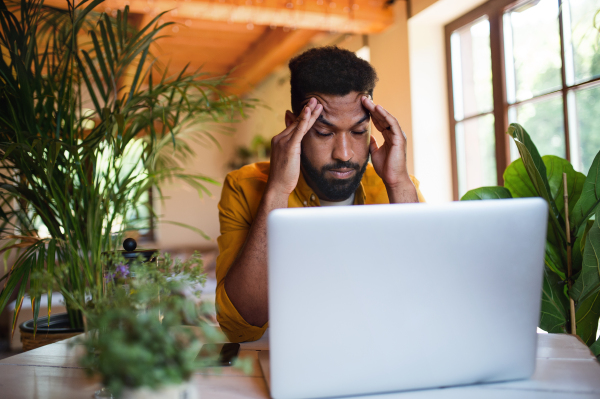 Portrait of frustrated young man with laptop working indoors, home office concept.