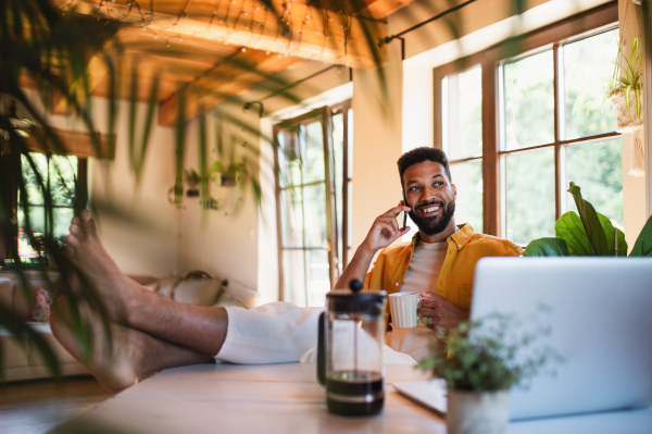 A young man with laptop and coffee working indoors, home office concept.