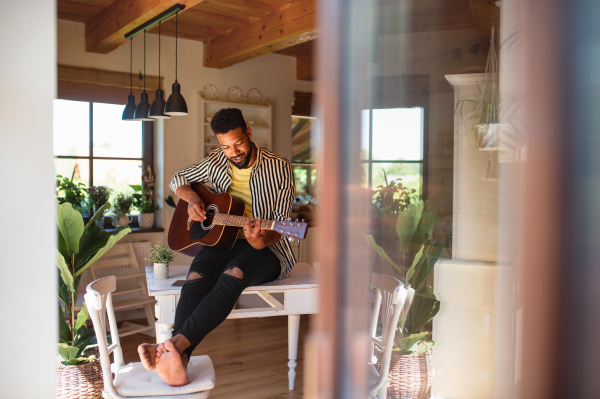 Portrait of happy young man with guitar indoors at home, relaxing.