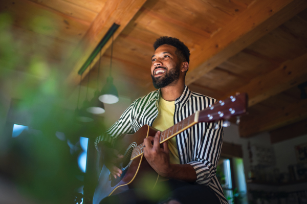 Portrait of happy young man with guitar indoors at home, relaxing.