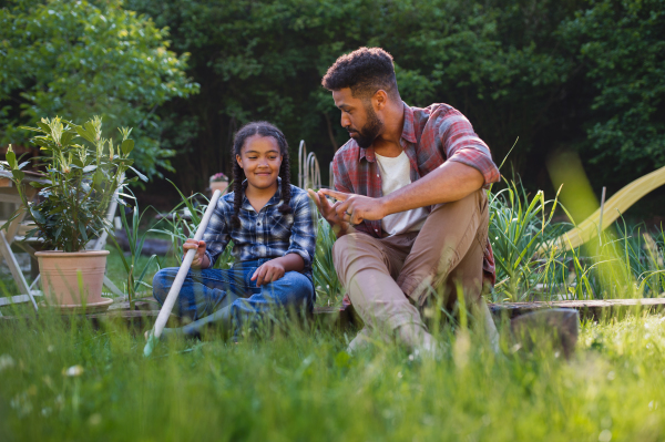 Happy young father with small daughter working outdoors in backyard, a gardening concept.