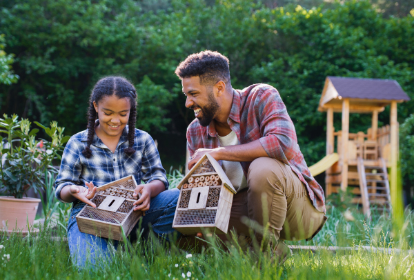 A happy young man with small sister holding bug hotels outdoors in backyard, laughing.