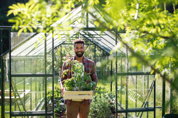 Portrait of happy young man working outdoors in backyard, gardening and greenhouse concept.