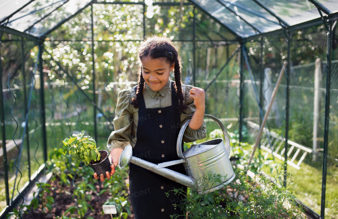 A happy small girl gardening in greenhouse outdoors in backyard.