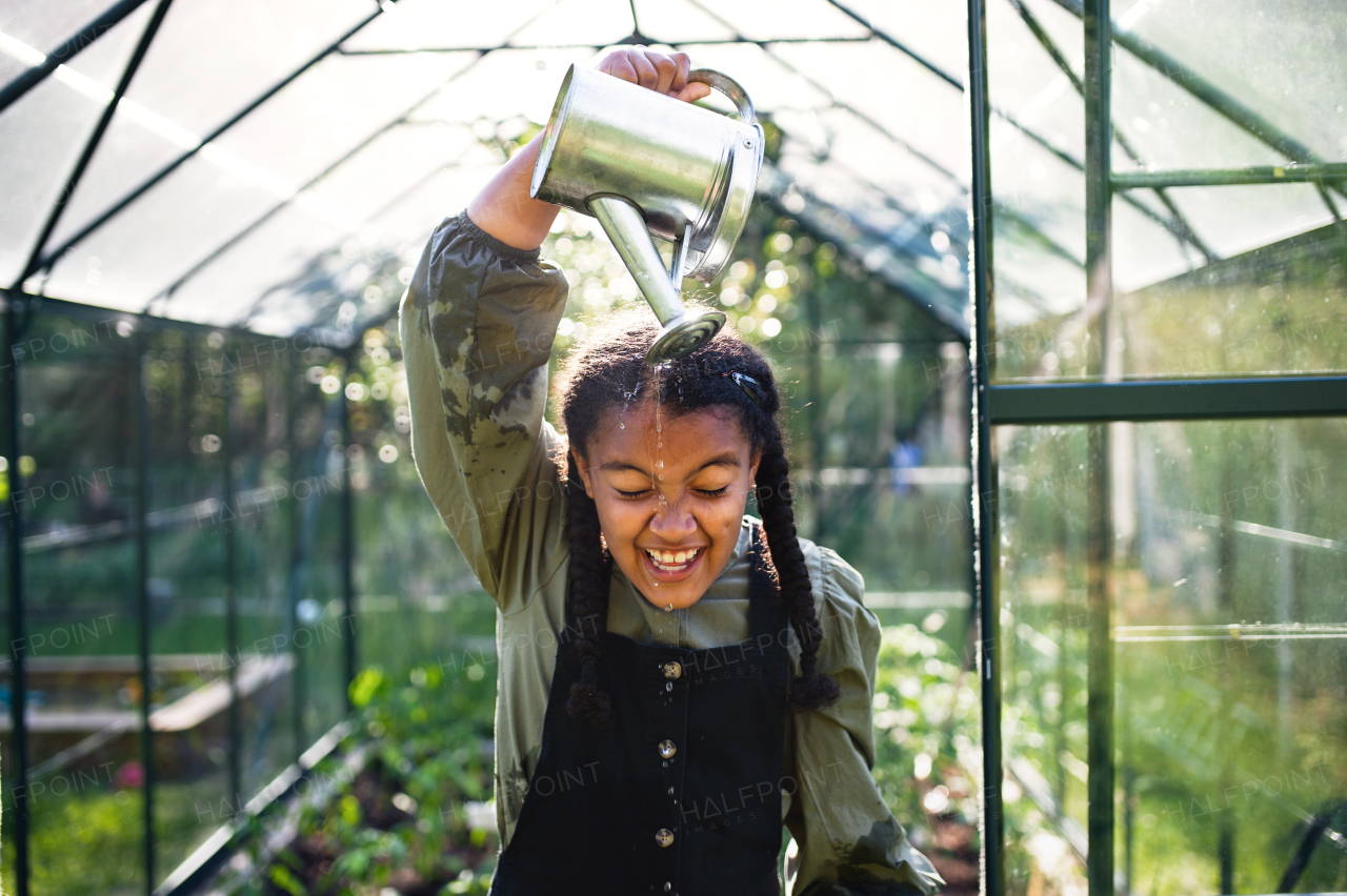 A happy small girl gardening in greenhouse outdoors in backyard, having fun.