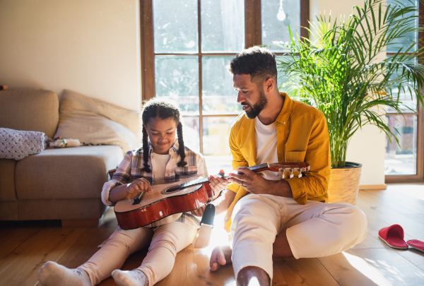 Front view of small girl with big adult brother indoors at home, playing guitar.