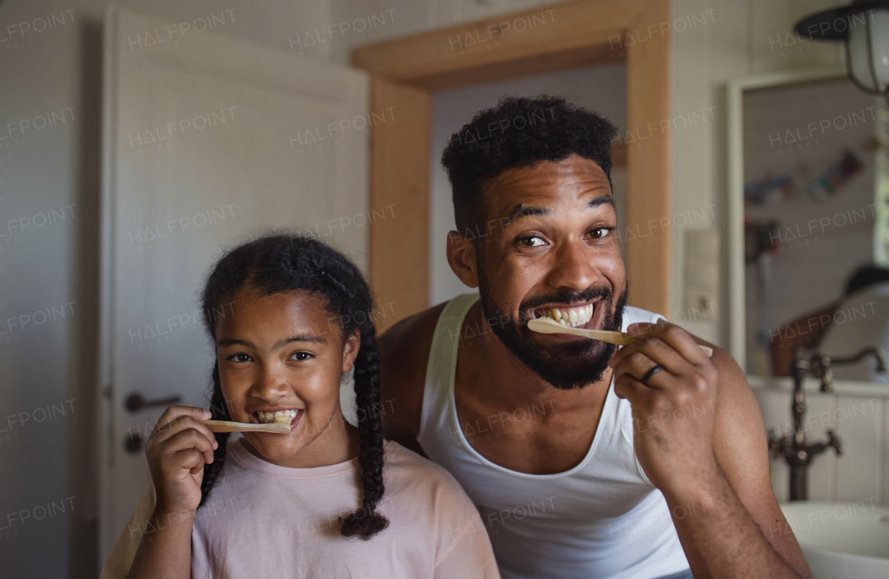 A happy young father with small daughter brushing teeth indoors at home, sustainable lifestyle.