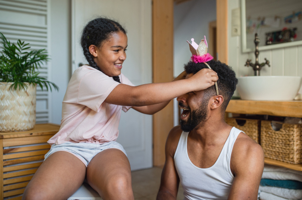 A happy young father with small daughter indoors at home, having fun in bathroom.