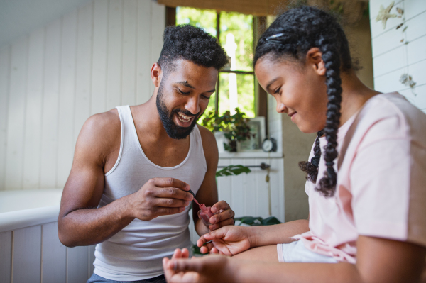 A happy young man with small sister indoors at home, painting nails in bathroom.