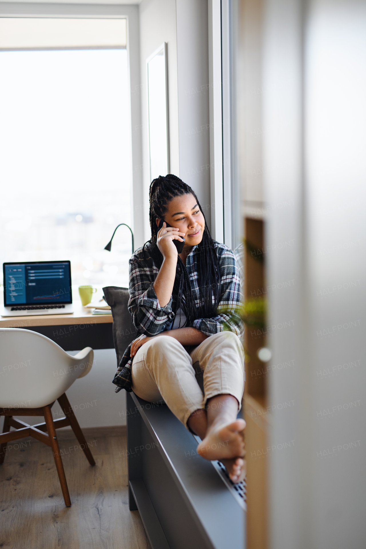 A portrait of happy teenage girl student sitting indoors in bedroom at home, using smarpthone.