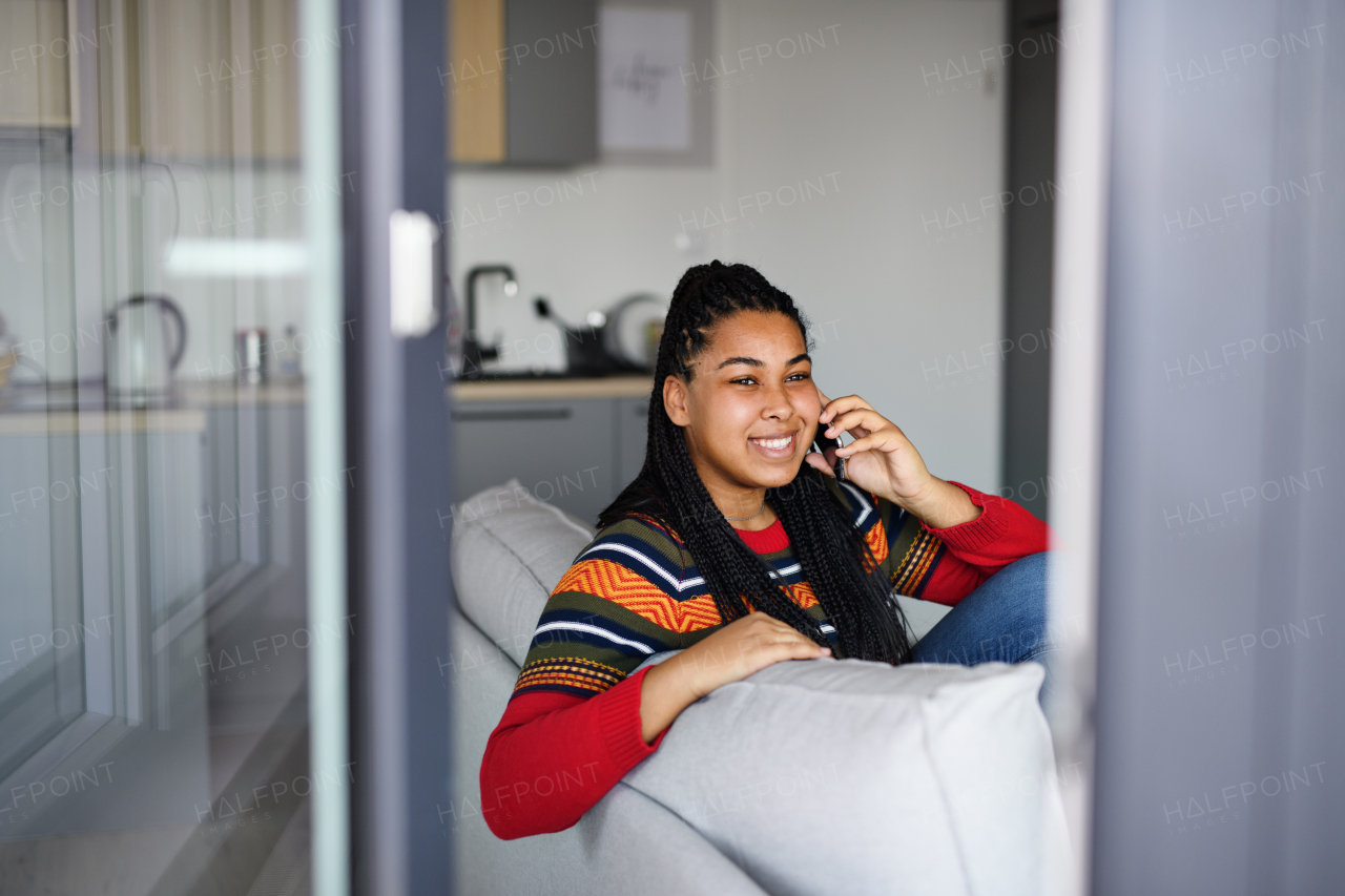 A happy teenage girl student on sofa indoors at home, using smartphone.