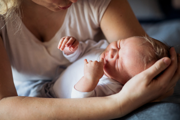 A midsection of unrecognizable mother holding a sleeping newborn baby at home.