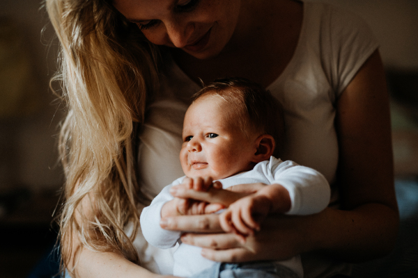 A beautiful young mother holding a newborn baby at home, midsection.