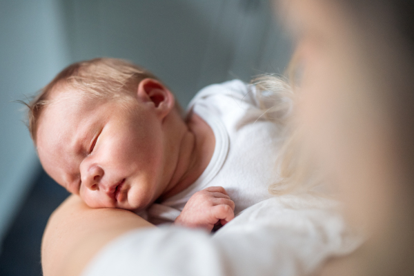 A close-up of unrecognizable mother holding a sleeping newborn baby at home.