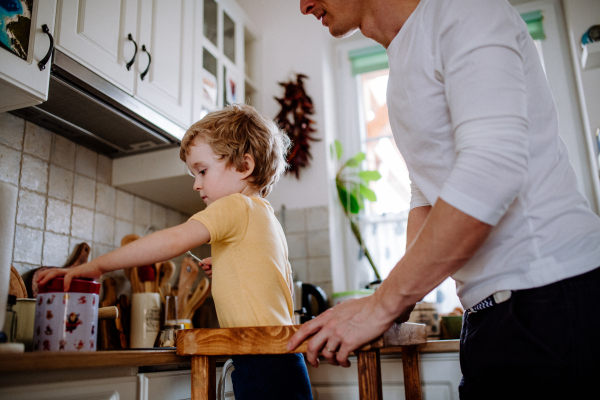 An unrecognizable father with a toddler son spending time in a kitchen at home.