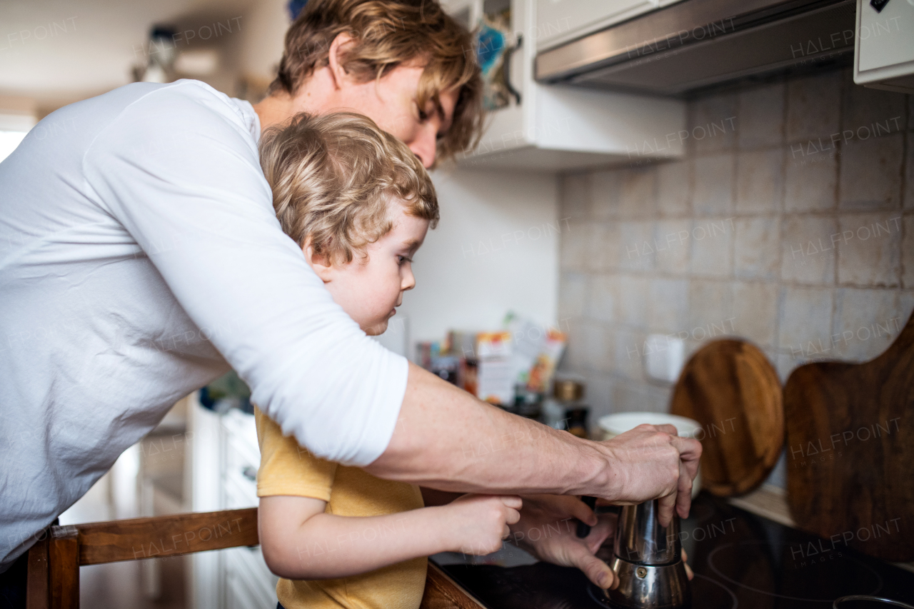 A young father with a toddler son spending time in a kitchen at home.