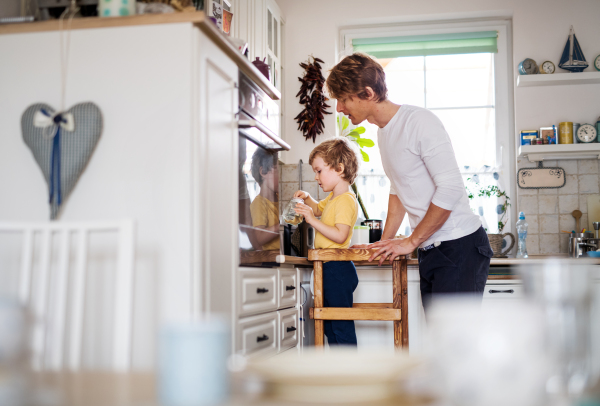 A young father with a toddler son spending time in a kitchen at home.