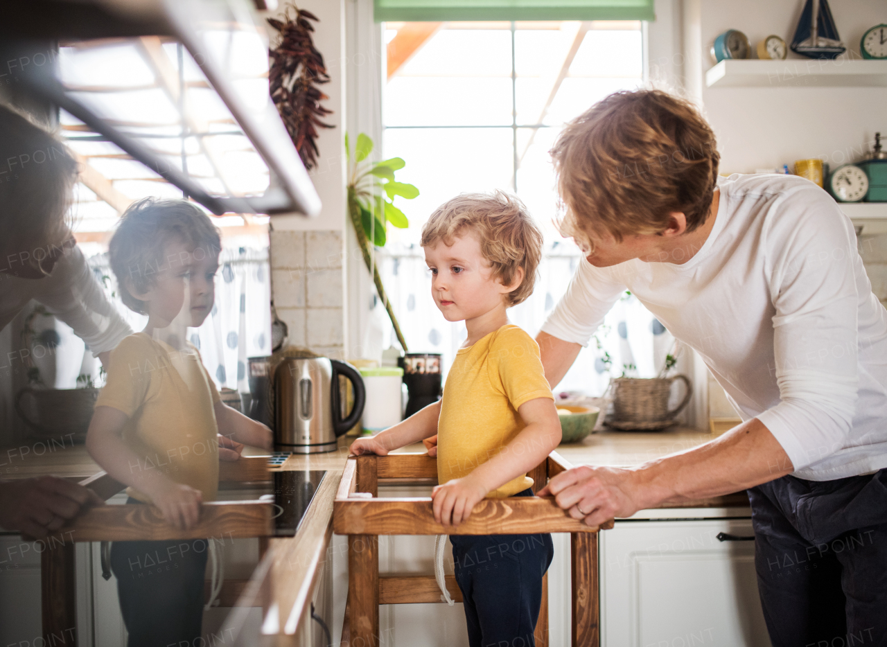 A young father with a toddler son spending time in a kitchen at home.