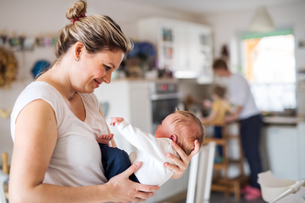 A beautiful young mother holding a newborn baby in kitchen at home.