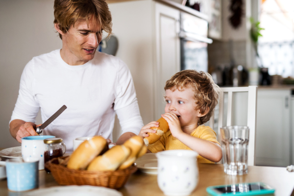 A young father with a toddler son eating breakfast indoors at home.