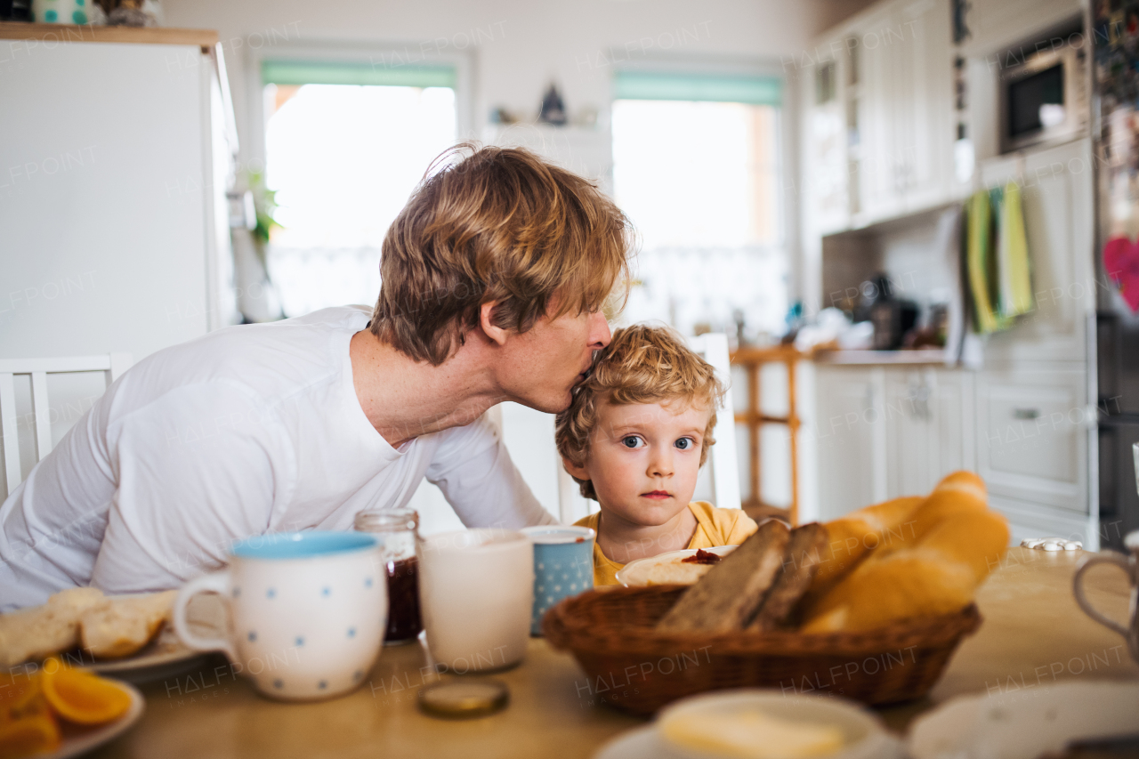 A young father with a toddler son eating breakfast indoors at home.