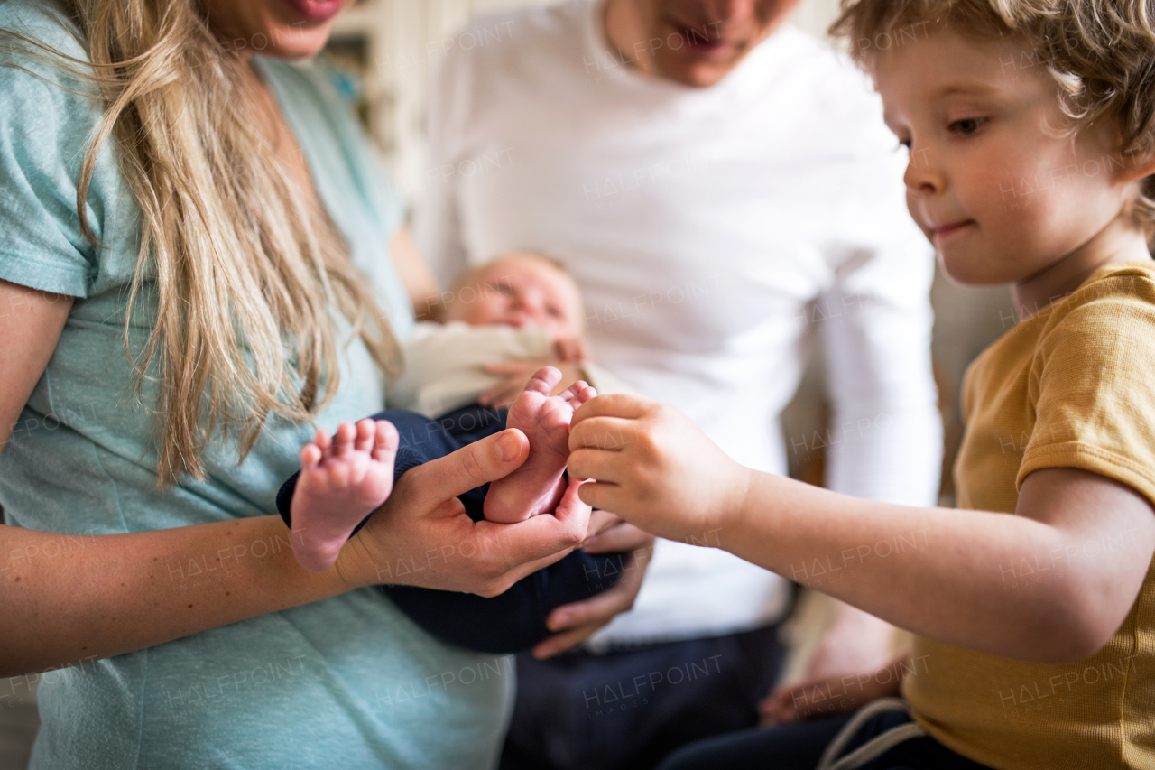 A midsection of parents with a newborn baby and small toddler son at home.