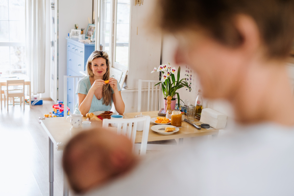 Beautiful young parents holding a newborn baby at home, eating breakfast.