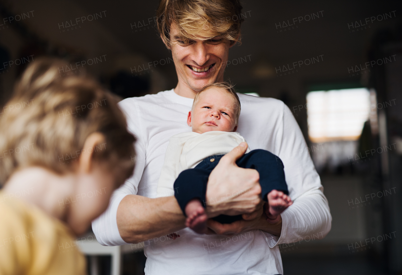 A young father holding a newborn baby and toddler son at home.