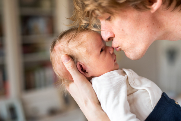 A close -up of young father holding a newborn baby at home, kissing him.