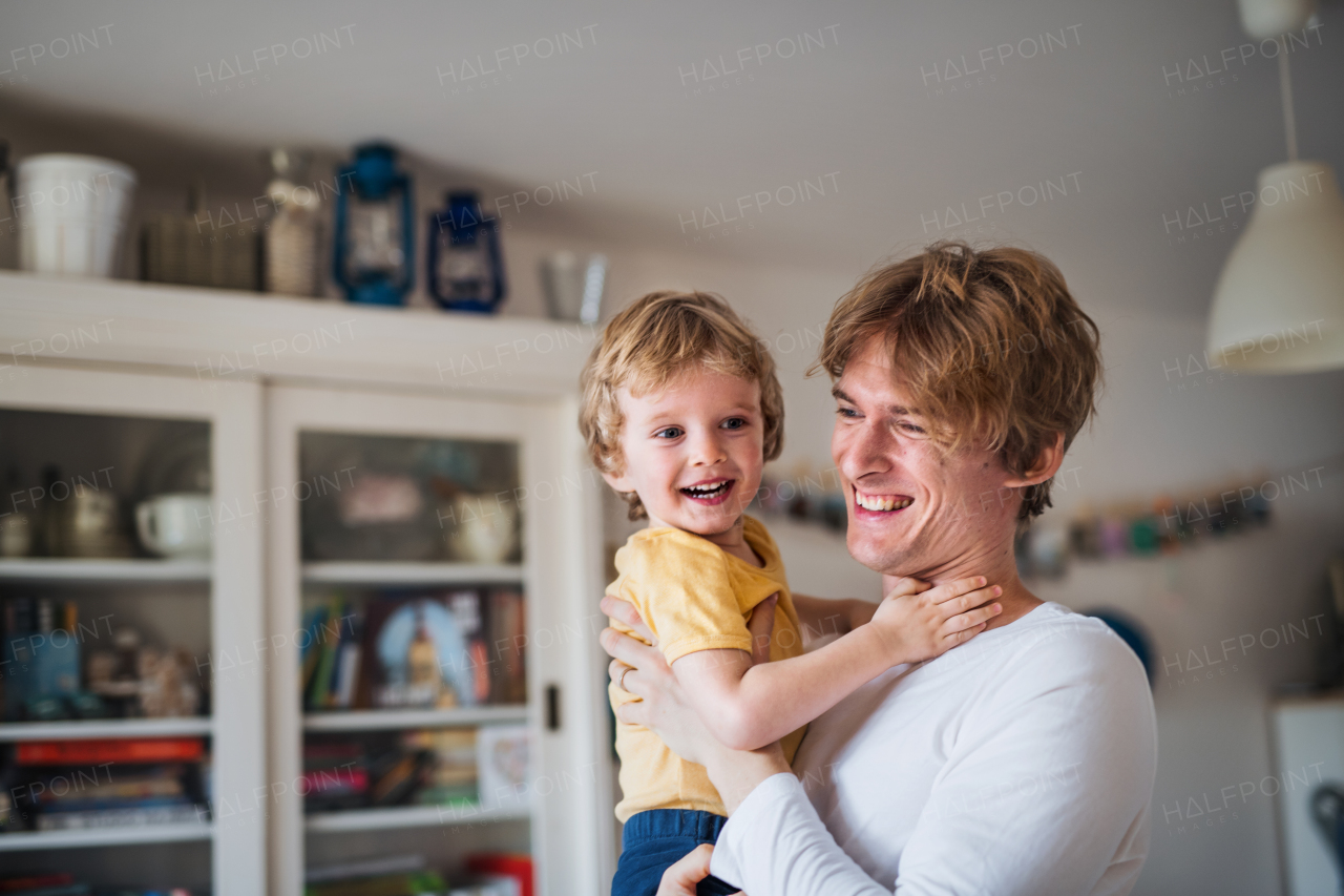 A happy father holding a toddler son at home.