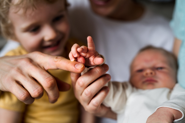 A midsection of father with newborn baby and small toddler son at home.