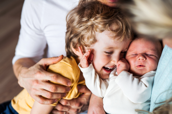 A midsection of father with newborn baby and small toddler son at home.