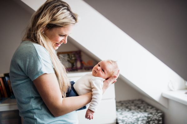 A beautiful young mother holding a newborn baby at home.