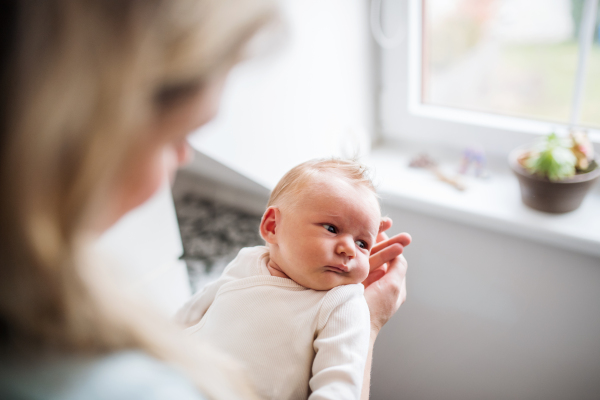 A midsection of unrecognizable mother holding a newborn baby at home.